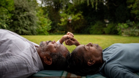 A man and woman lie in a field holding hands