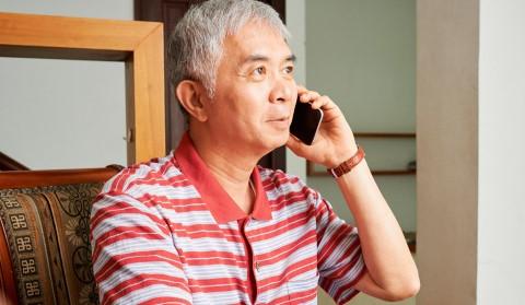 A man sits at home on the phone looking optimistic 
