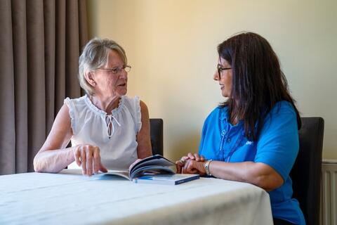 A dementia adviser and a person sit at a table looking at a booklet